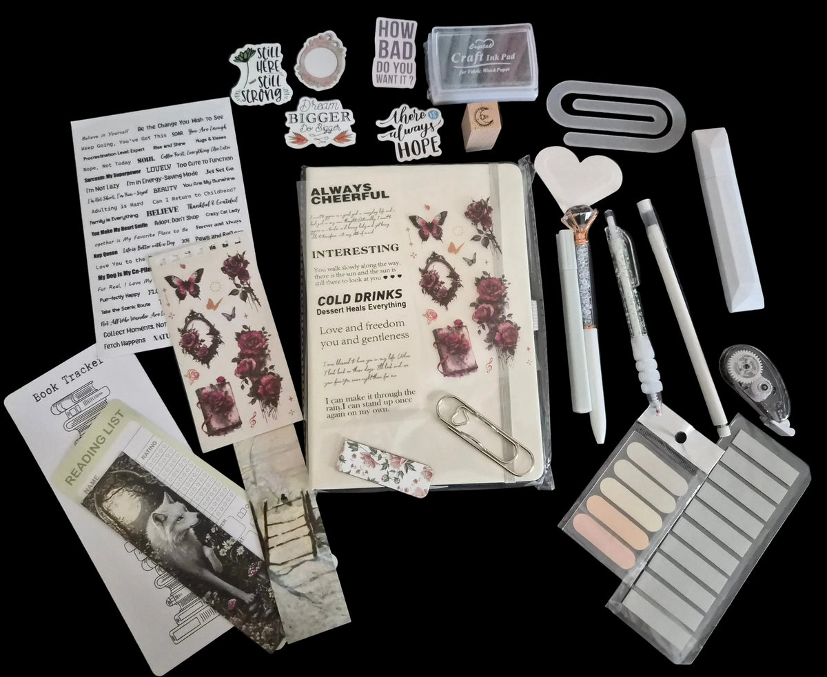 A flat-lay arrangement of various stationery and scrapbooking supplies including a notepad, stickers, paperclips, pens, a heart-shaped tool, a palette, and other accessories